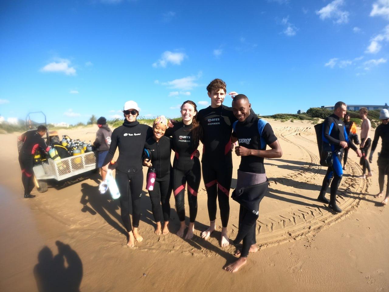 Interns in wetsuits on the beach after a survey dive