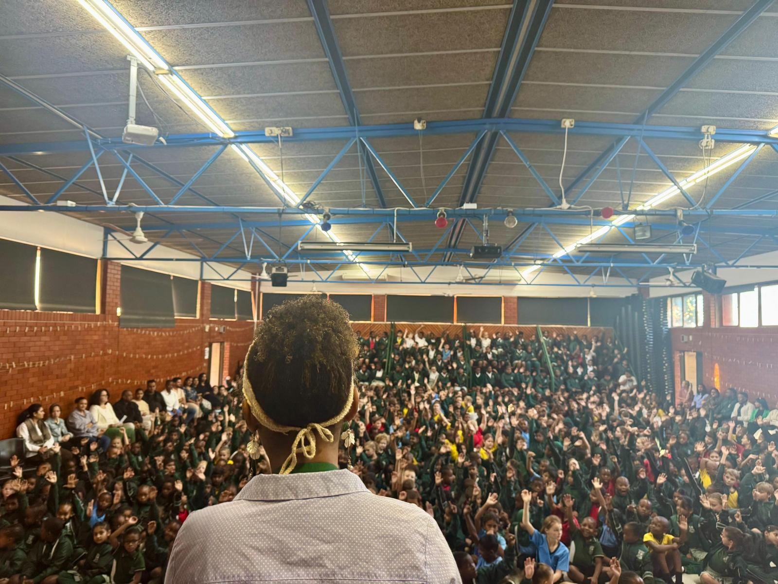 An intern addressing a school hall packed with learners raising their hands